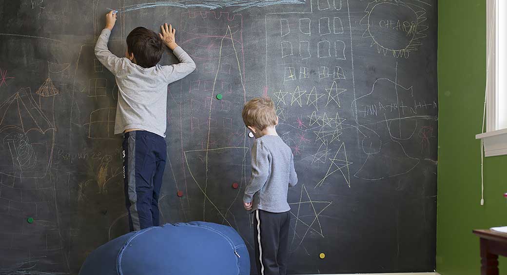 Two Young Boys Drawing on a Chalkboard Wall