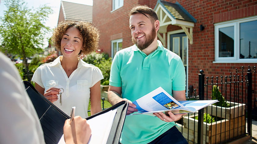 Couple talking to a real estate agent in front of a house