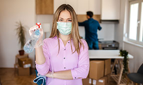 Young Woman Wearing a Mask for COVID-19 protection While Disinfecting Her New House