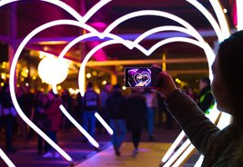 Woman Taking Picture of Heart Shaped Lights in a City Street - NEA Discount Tickets Program
