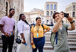 NEA Travel: Guided Tours - Tourists taking photos with tour guide in front of Duomo as they explore Milan, Italy