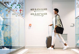 Young Woman Walking with Wheeled Luggage in Hotel Corridor