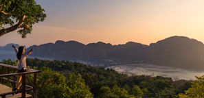 A woman standing at Phi Phi View Point with a bird's eye view of the mountains, the sea and the sunset in Thailand.