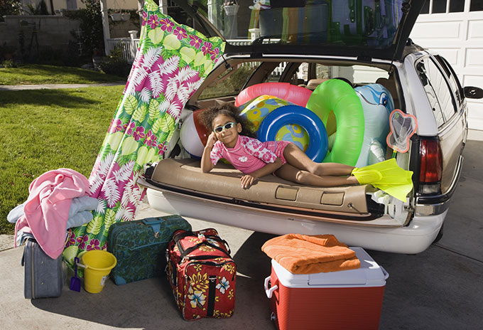 Young girl in beach gear sitting in back of packed car