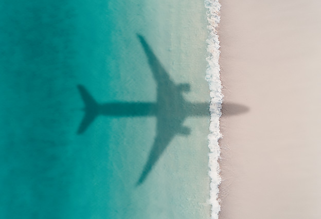 NEA Travel: Airfare - Aerial Shot Showing an Aircraft Shadow Flying Over an Idyllic Beach