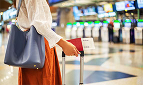 NEA Travel: Airfare - Woman at check-in counter in airport terminal, with luggage and passport