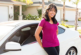 Woman smiling while she leans against her car in front of her home