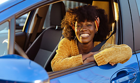 Smiling African-American Woman Sitting in the Driver's Seat of a Blue Car