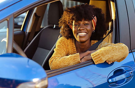 Smiling African-American Woman Sitting in the Driver's Seat of a Blue Car