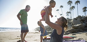Family on the beach with mother in the foreground holding up her toddler