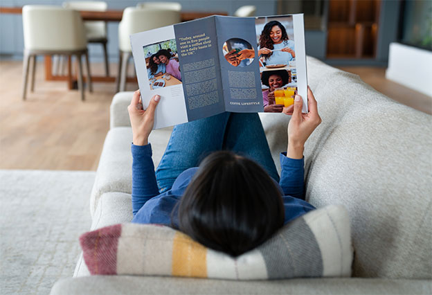 NEA Magazine Service - Woman relaxing at home reading a magazine while lying down on the sofa.