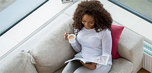 NEA Magazine Service - Woman relaxing at home while reading a magazine on the sofa.