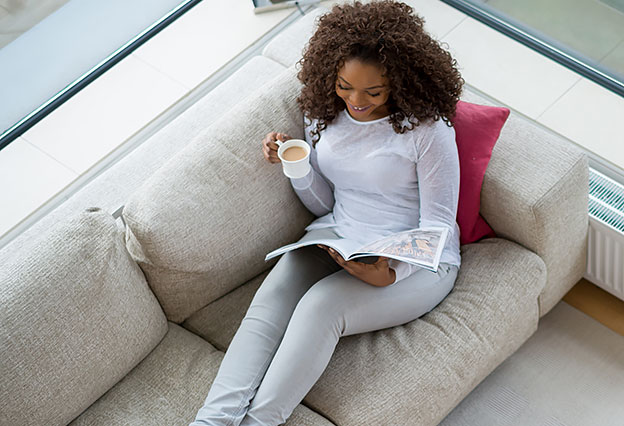 Happy Woman Relaxing at Home Reading a Magazine While Sitting on a Sofa - NEA Magazine Service