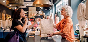 Female owner giving a bag to a female customer at checkout in a store