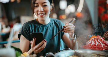 Asian Woman Using Smartphone While Enjoying Chinese Hotpot in a Restaurant