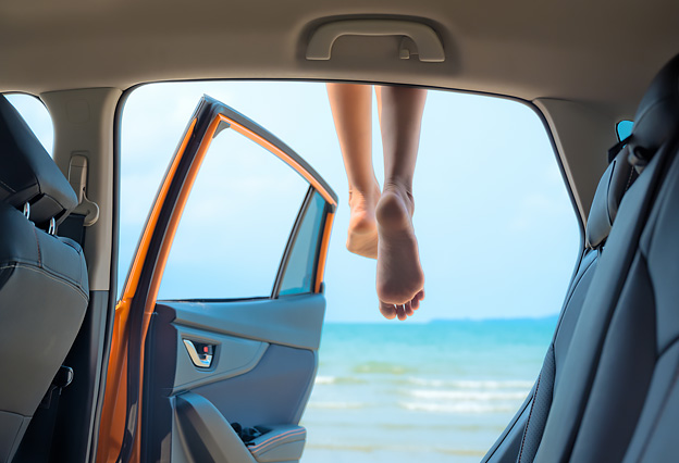 NEA Travel: Car Rental - Woman Sitting on Top of a Car, Legs Dangling Over the Edge, Overlooking a Beach