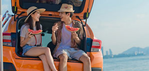 NEA Travel: Car Rental - Parked on the waterfront with the hatchback up, a couple happily enjoy a sunset picnic.