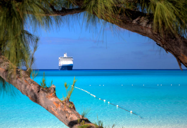 NEA Travel: Cruises - View of a ship waiting on the horizon from a beautiful  blue water beach in the Caribbean.