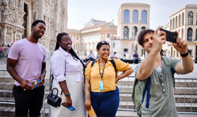 NEA Travel: Guided Tours - Tourists taking photos with tour guide in front of Duomo as they explore Milan, Italy
