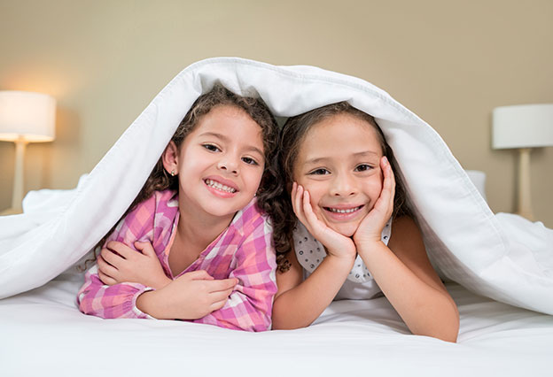 Little girls smiling underneath big hotel bed covers