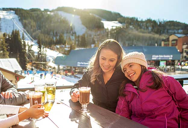 NEA Travel: Resorts - Mother and daughter laughing and having drinks outside at a ski resort