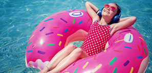 NEA Travel: Resorts - Little girl is enjoying the sunshine on a bright doughnut-themed raft while floating in the water and listening music.