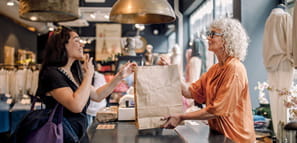 A sales clerk hands bag to customer at checkout