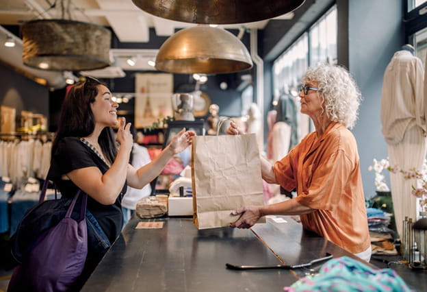 A sales clerk hands bag to customer at checkout