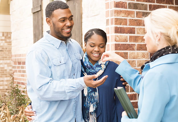 Una joven pareja recibe de su agente inmobiliario la llave de su primera casa