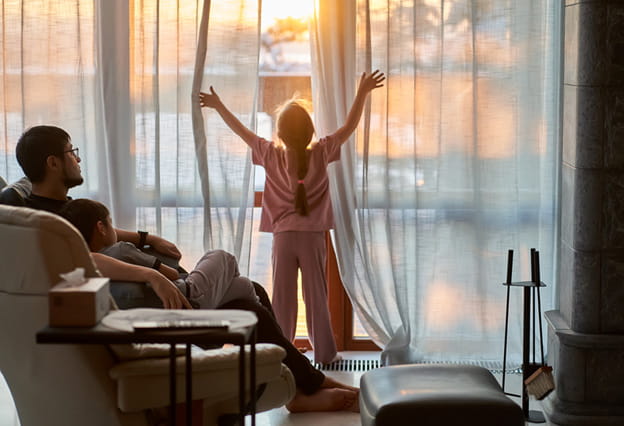 La niña abre las cortinas de una gran ventana panorámica e ilumina la habitación con la cálida luz del atardecer