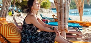 Joven asiática disfrutando de un momento relajante, sentada en un banco junto a la playa