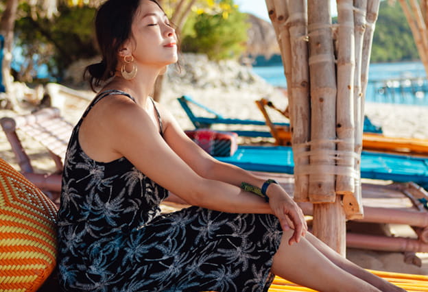 Joven asiática disfrutando de un momento relajante, sentada en un banco junto a la playa