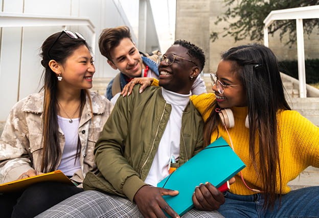 Un grupo de estudiantes universitarios habla y ríe sentados en las escaleras del campus afuera