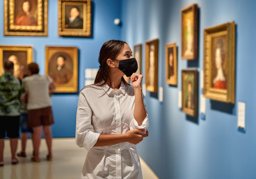 Una visitante con su máscara antivirus en el museo histórico viendo cuadros.