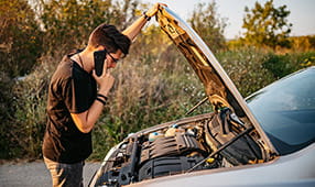 Joven mirando debajo del capó y llamando a asistencia en carretera