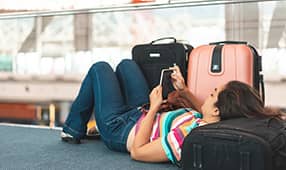 Turista cansado que usa equipaje como reposacabezas mientras espera en el aeropuerto