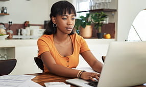 Mujer joven sentada con su computadora portátil y papeleo en casa