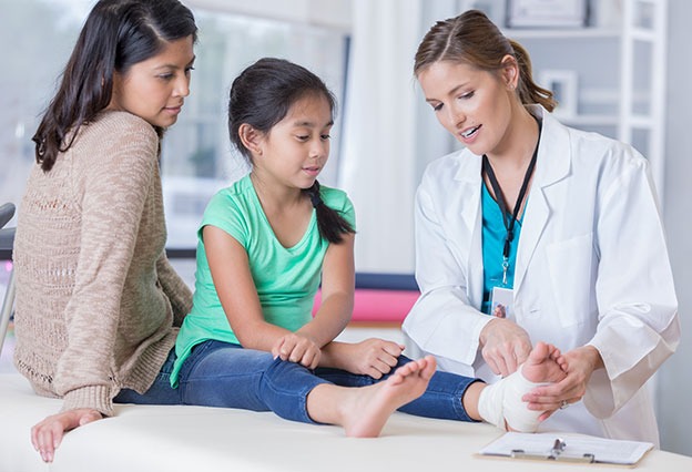Emergency room doctor talks with young girl and the girl’s mom about the girl’s injured ankle