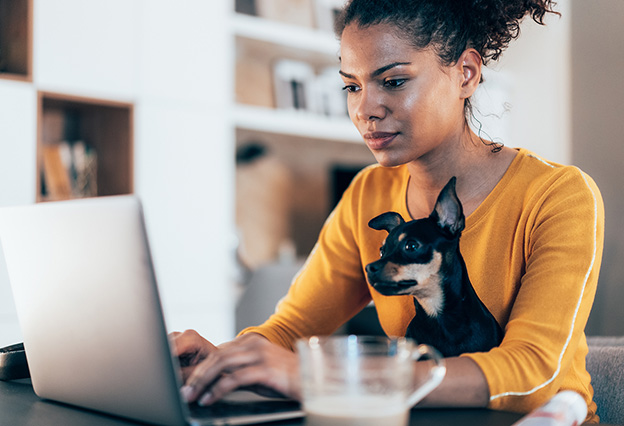 Young woman sitting with her pet dog and using laptop at home