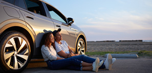 A man and a woman sitting against a car during sunset