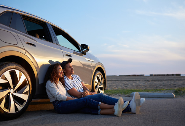 Un hombre y una mujer sentados frente a un automóvil durante la puesta de sol