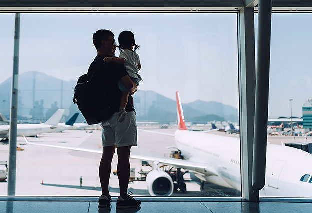 Silhouette of father embracing daughter and looking at airplane through window at the airport