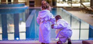 Hermano y hermana tomados de la mano usando batas de baño mientras están de pie junto a la piscina en el hotele