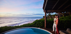 Dos chicos parados junto a la piscina viendo el amanecer en una lujosa villa tropical con vistas a la playa y al océano
