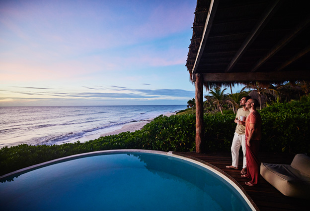 Two guys standing poolside watching sunrise at luxury tropical villa overlooking beach and ocean