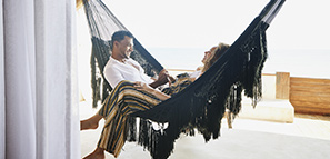 Smiling couple holding hands while sitting in hammock