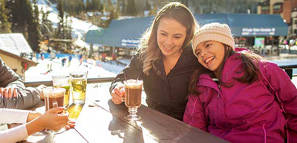 Madre e hija riendo y tomando bebidas en una estación de esquí